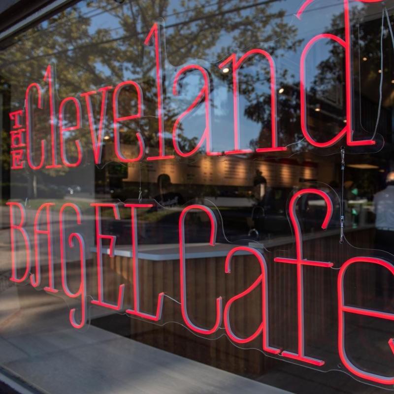 A neon sign in a window reading "The Cleveland Bagel Cafe"
