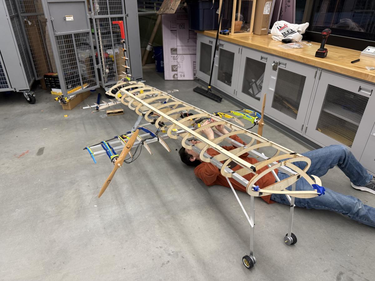 Male student from Kent State's Design, Build, Fly team lays underneath the framework of the team's aircraft to make adjustments.