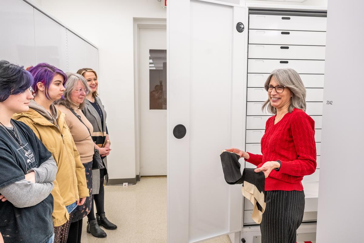 Woman with red long-sleeve shirt and glasses, showing an object to a small crowd