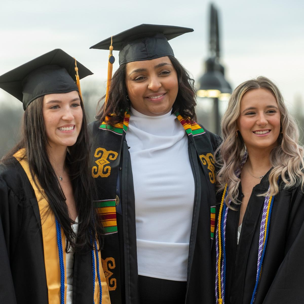 Three graduating students in their cap and gowns smiling at something off camera