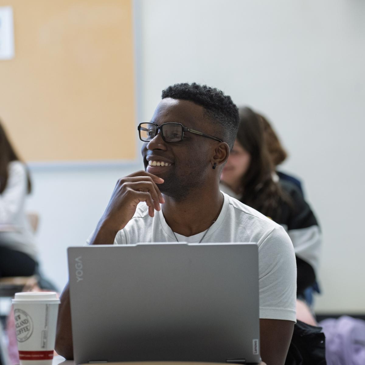 A male student sitting at a classroom desk with his laptop open