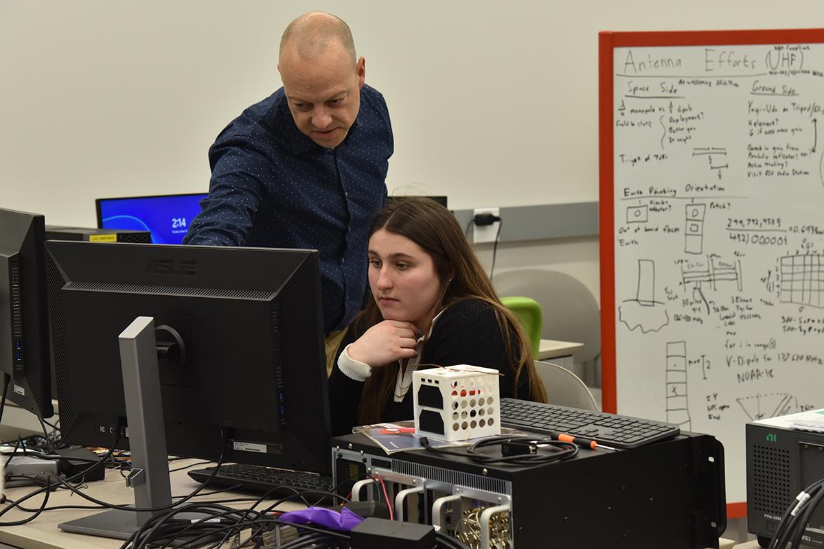 A young woman observes a computer screen while an older man points to a specific spot on the screen