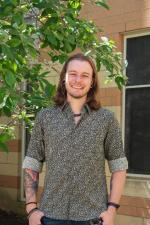 Outside Headshot of Benjamin Hunsicker in front of a brick building and a tree