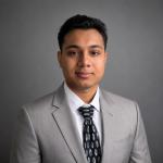 Portrait of Nufath Arham wearing a gray business coat and black tie. 