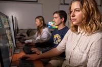 �������� student femail dresses in a cream button up shirt sits in front of a computer screen. 