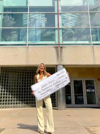 McKenzie Morgan holding a large check in front of Rockwell Hall.
