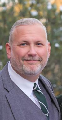 Michael Foster in a grey suit jacket posed for a headshot