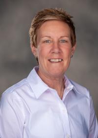 Professional headshot of Missy Hatch wearing a light-colored collared shirt against a neutral gray background.