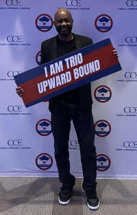 Lewis Williams smiling at the camera holding a sign that reads I Am Trio Upward Bound