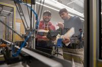 Two students examine the workflow between two autonomous manufacturing robots