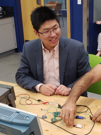 A man sitting at a table, working on a STEM project. You can see another man's arm reaching into the frame.