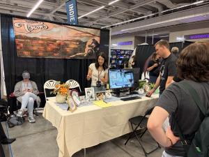 Attendees interact with an independent game booth at the Cleveland Gaming Classic, where a game is displayed on a monitor alongside artwork and promotional materials.