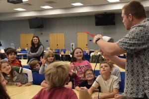 Young students gathered in a large hall watching a STEM demonstration