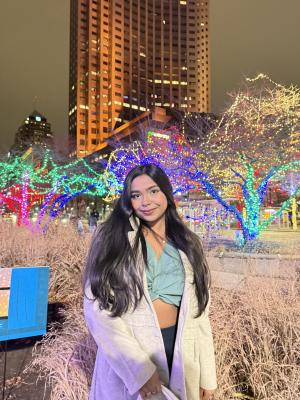 Shashwati Sikder Sharaya posing for picture in front of a building with lights in the background. 