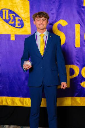 Cameron Paladenic posing in front of the PSE purple and gold flag National Sports Selling competition.