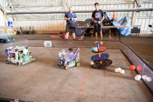 Two students control two battle robots against each other in a low arena