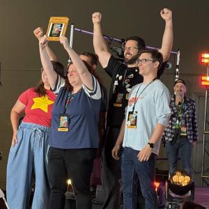 A group of game creators celebrates onstage at the Cleveland Gaming Classic as one person raises an award plaque overhead.
