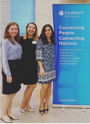 Romanian Fulbright scholars pose next to a 'Fulbright Romania' standing poster.
