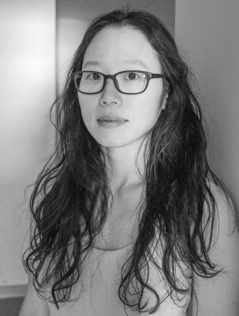 Black and white portrait of Aimee Lee, a woman with long dark hard and black glasses. 