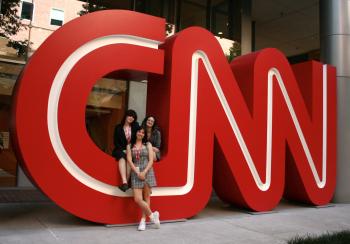 Three student media students pose in front of a large CNN logo