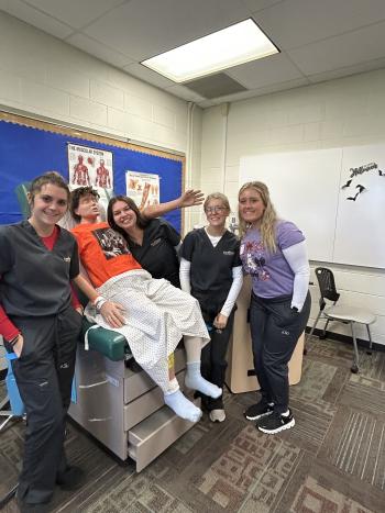 Medical Assisting students pose with a patient simulation manikin in the classroom
