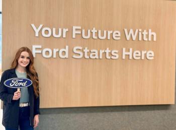 �鶹��ѡalumna Jacqueline stands next to a sign at the Ford company in Detroit that reads "Your Future With Ford Starts Here"