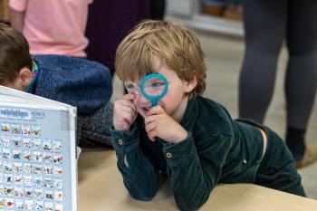 A kindergartner looks through a small magnifying glass