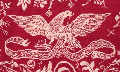 Detail of red fabric with a white eagle created with thread. 