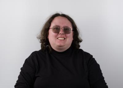 A young woman with short brown hair and tinted glasses wearing a black turtle neck