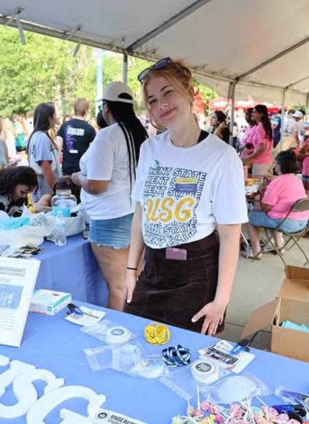 Kent State University Honors College student Sofia Sprain stands near a table for Undergraduate Student Government during an event.