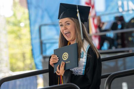 A happy 51±¬ÁÏ graduate holds her di A happy 51±¬ÁÏ graduate holds her diploma during the university’s spring 2023 commencement ceremony.
