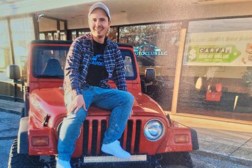 Michael Leposa sits on red Jeep wrangler