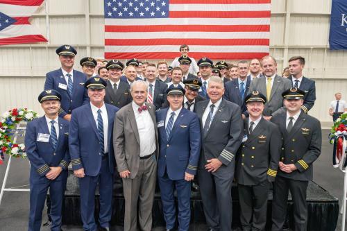 Students and alumni dressed professionally in front of an American flag. 