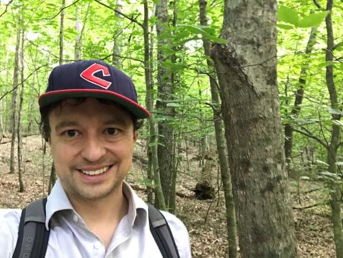 Ryan Dezember stands in a wooded area wearing a baseball cap