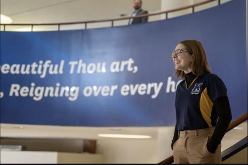 Ella stands on the staircase inside the Student Center, with words from the alma mater displayed behind her.