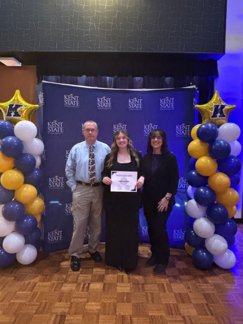 Isabella accepts an award standing in front of a display of balloons.