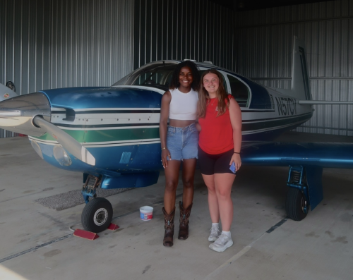 Isabella (right) poses with a classmate in front of a small plane in the hangar.