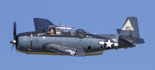 A WW2-era navy bomber flies against a blue sky