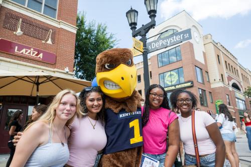 Four students posing with the �Ը������� mascot in downtown Kent.