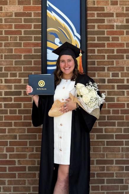 A young woman dressed for graduation holding a diploma and a bouquet of white flowers