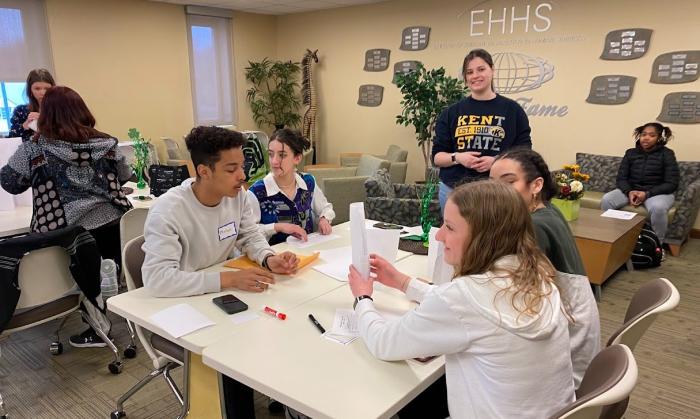Allison Coneglio stands behind students seated at a table