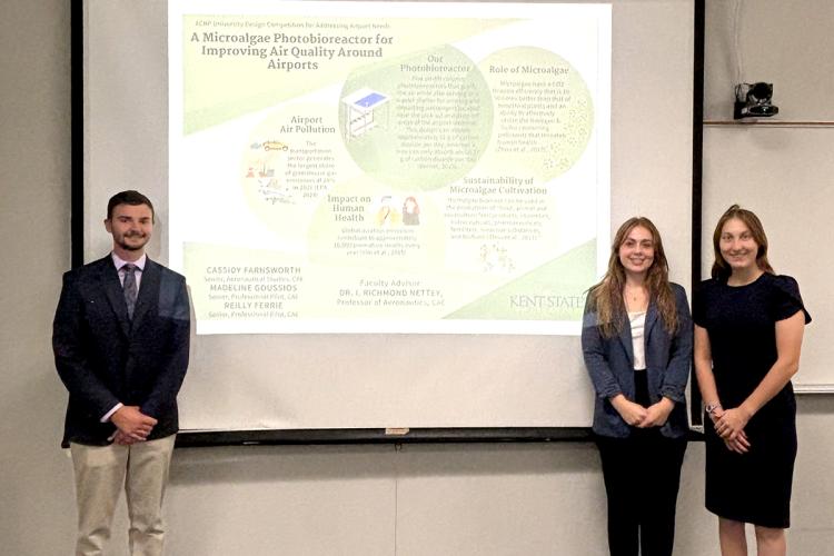 A large projected poster is flanked by one male student to the left and two female students to the right