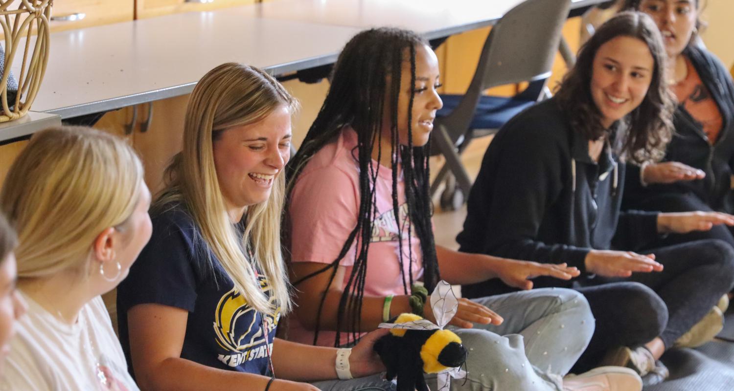 Early Childhood Education students sitting in a circle on the floor laughing during a music demonstration class.