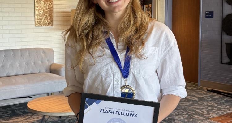 Rebecca LaGuardia standing for a photo while holding a Flash Fellow certificate. 