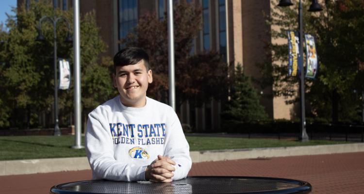 Asadbek Masharipov sitting at a table outside on the ���ϲ����� campus. 