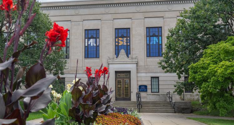 Light beige building with "Museum" showcased on its front and red flowers framing the image