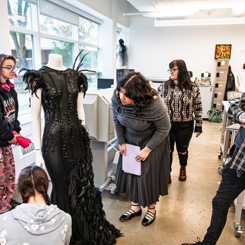 Group of students study a black garment in a fashion studio. 