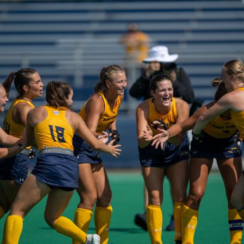 Members of Kent State’s field hockey team laugh and smile together on the field.