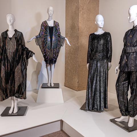 Four mannequins pose in various sparkling, dark chrome outfits