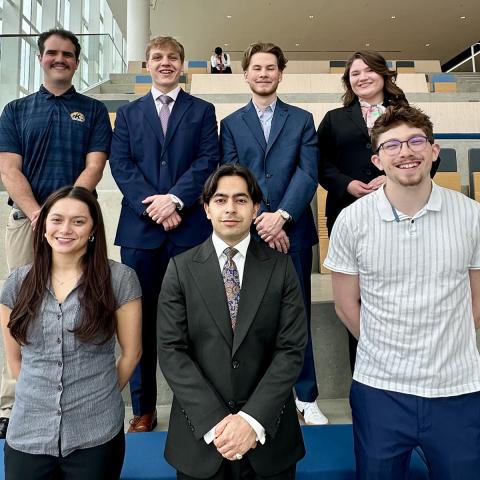 eight student ambassadors standing on a staircase in Crawford hall in business attire smiling at the camera.